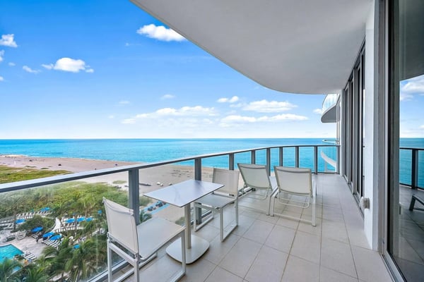 Oceanfront balcony with dining table, lounge chairs, and panoramic turquoise water and beach view
